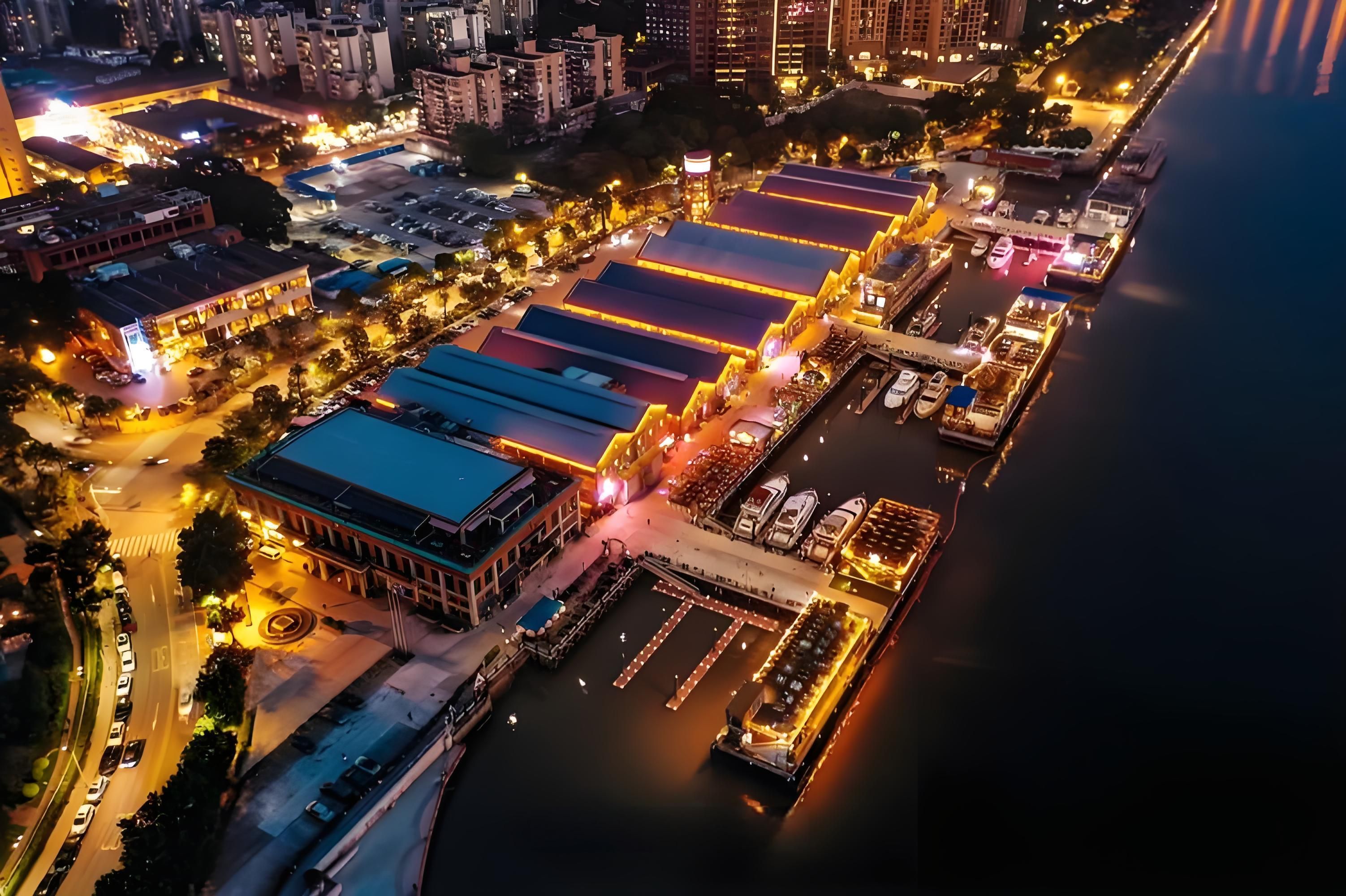 An aerial view of a waterfront area with buildings, a marina, and a road.