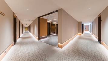 A long, narrow hotel corridor with a patterned carpet, recessed lighting, and a mirrored wall reflecting the corridor.