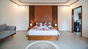 A modern bedroom with a wooden bed, two bedside tables, a sofa, and a coffee machine. - Pertibi Private Villa (Ubud)