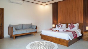 A bedroom with a wooden bed, a grey sofa, and a white circular rug. - Pertibi Private Villa (Ubud)