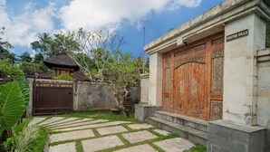 A courtyard with a stone pathway, a wooden gate, and a large ornate door. - Pertibi Private Villa (Ubud)