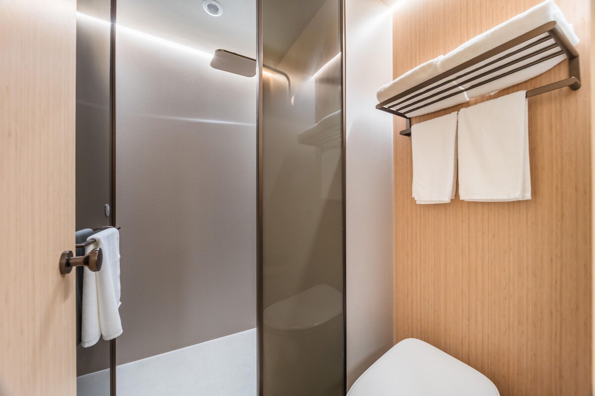 A modern bathroom with a glass shower enclosure, a toilet, and a towel rack with two towels.