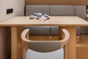 A modern dining area with a wooden table, grey cushioned seating, and a small tea set. - Ji Hotel Guangzhou Jiangnanxi Metro Station (Guangzhou)