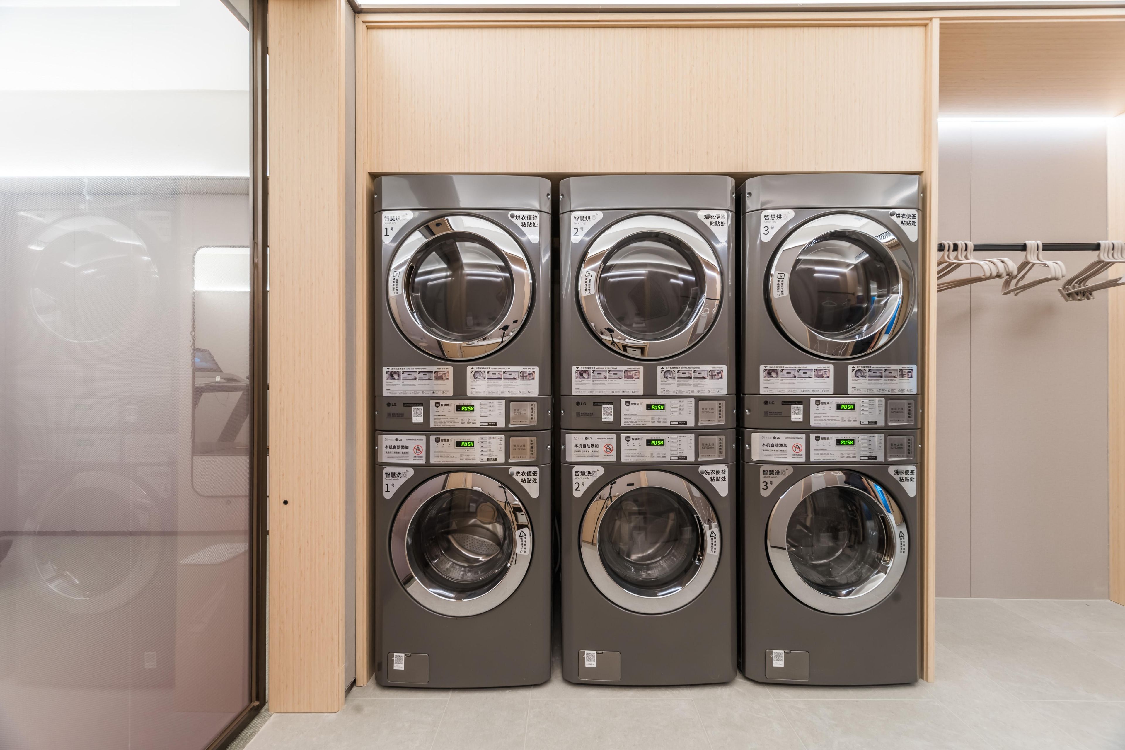 A row of three stacked front-loading washing machines in a commercial setting.