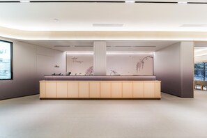 A reception area with a wooden counter, a large window, and a wall with abstract art. - Ji Hotel Guangzhou Jiangnanxi Metro Station (Guangzhou)