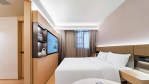Ein modernes Hotelzimmer mit einem großen Bett, einem Fernseher, einem Schreibtisch und einem Kleiderschrank.