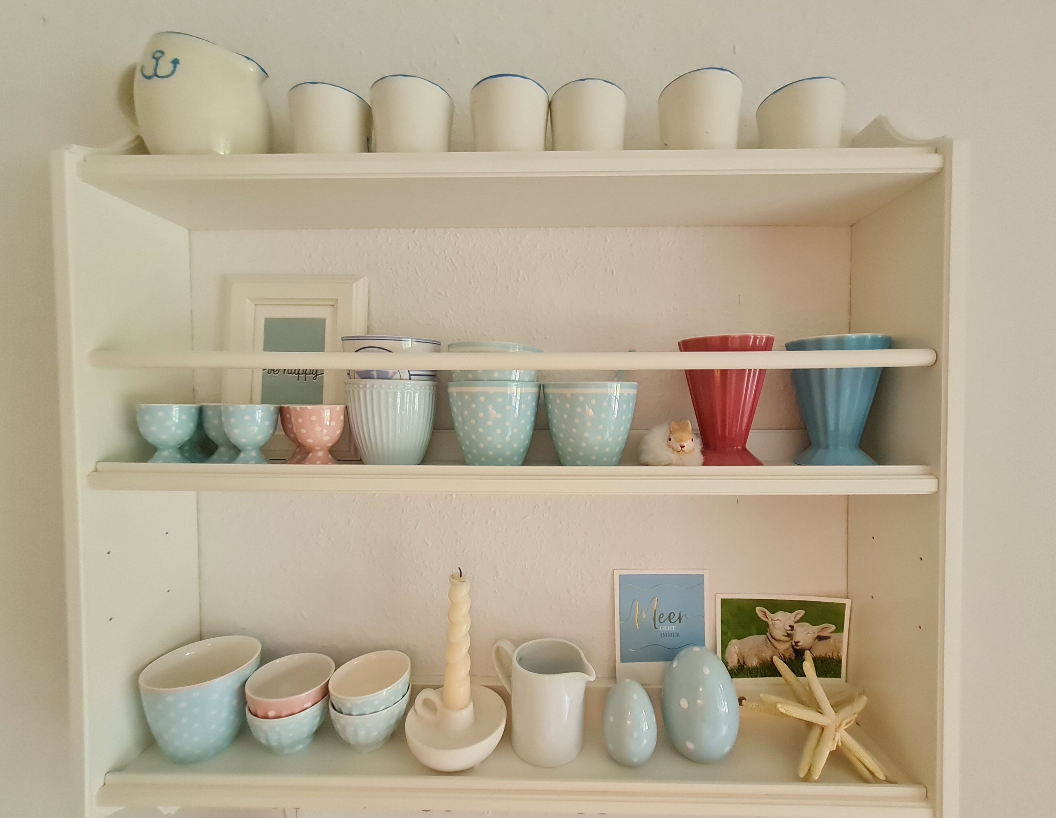 A shelf with various ceramic bowls and cups, a candle, and a framed picture.
