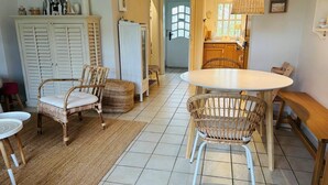 A cozy dining area with wicker chairs and a round table, a kitchen with a refrigerator and wooden cabinets, and a hallway leading to a door. - Comfortable house Landlust for 4 with garden and terrace in Garding (Garding)