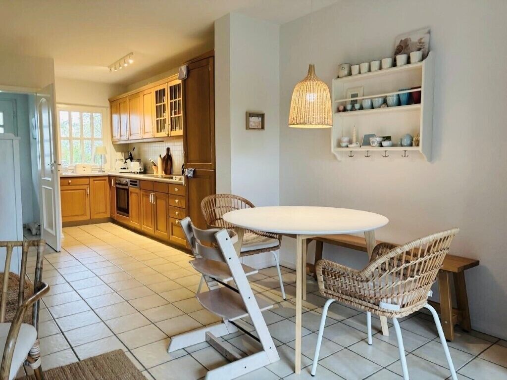 A kitchen with wooden cabinets, a round dining table, wicker chairs, and a hanging light fixture.