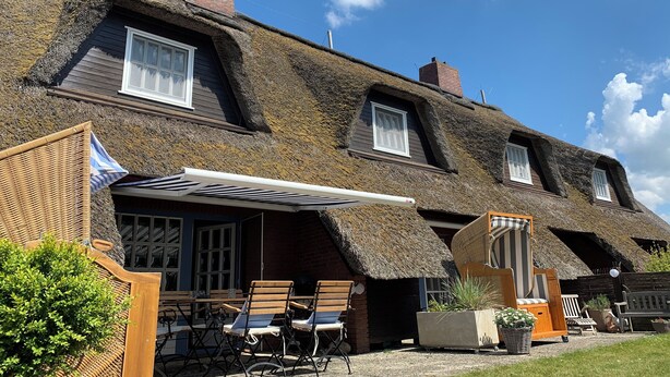 A traditional thatched-roof house with a covered patio area, wooden furniture, and a small garden. - Comfortable house Landlust for 4 with garden and terrace in Garding (Garding)