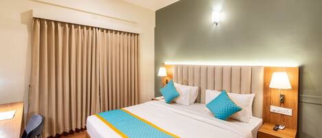 Habitación de hotel con una cama grande, dos mesitas de noche con lámparas, un escritorio con silla y una ventana con cortinas.