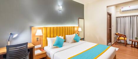A hotel room with a bed, desk, chair, and an air conditioning unit.