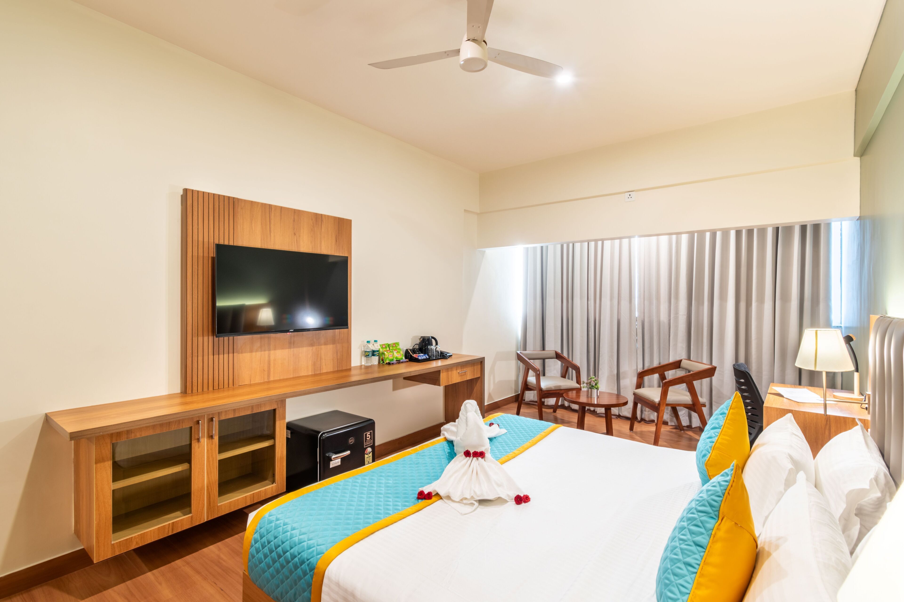 Habitación de hotel con cama, escritorio, televisión, silla y ventana con cortinas.