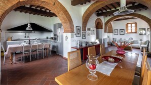 A spacious kitchen with a dining area, featuring exposed brick arches, wooden beams, and modern appliances. - Maria Gabriella Holiday Home  (Monticchiello)