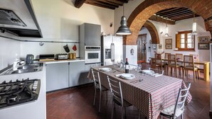 A kitchen with a gas stove, a refrigerator, and a dining area with a table set for four. - Maria Gabriella Holiday Home  (Monticchiello)
