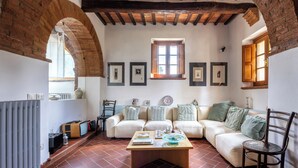 A cozy living room with a brick fireplace, a sofa set, a coffee table, and framed pictures on the wall. - Maria Gabriella Holiday Home  (Monticchiello)