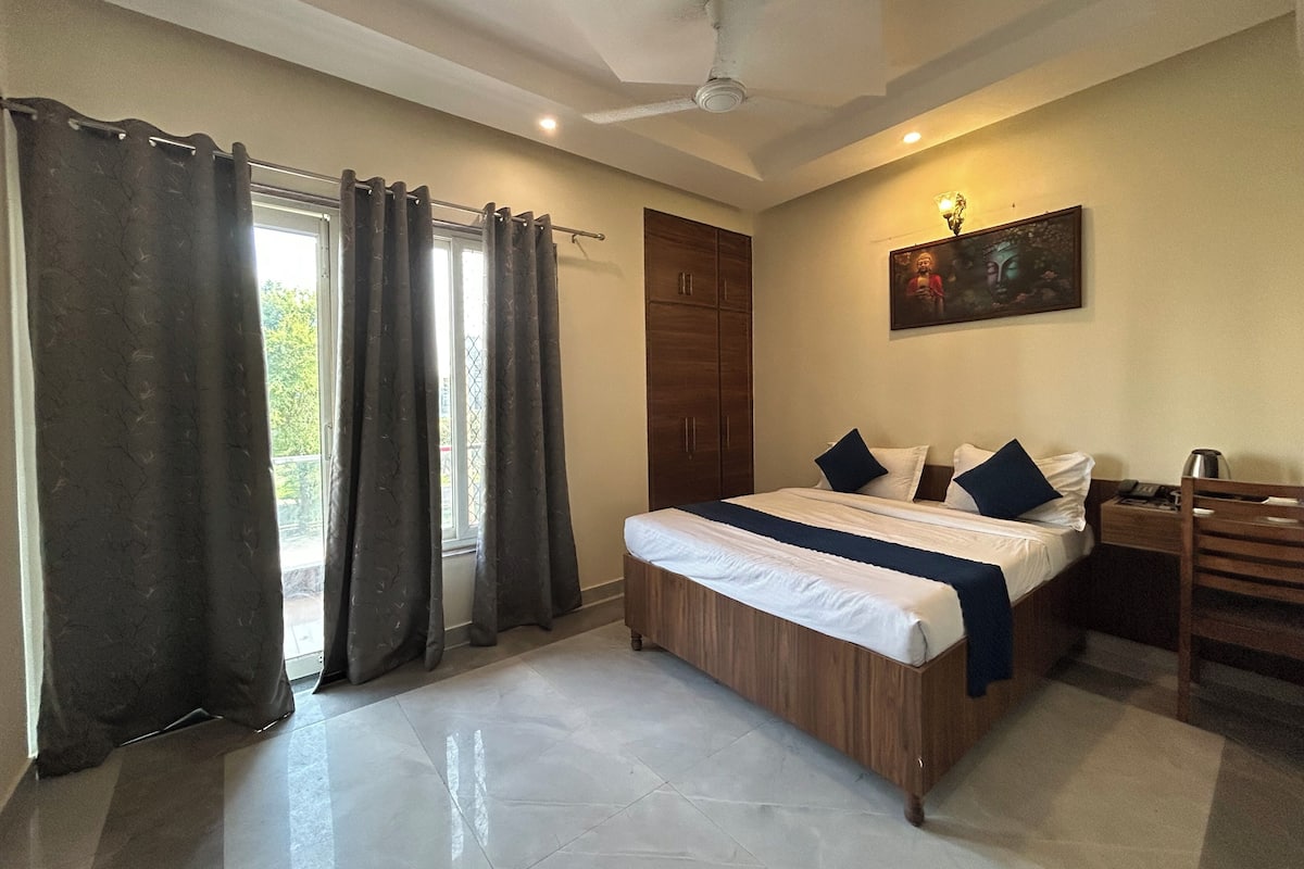 A bedroom with a bed, curtains, a ceiling fan, a nightstand, a lamp, and a painting on the wall.