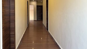 Un pasillo largo y estrecho con paneles de madera a la izquierda y una pared lisa a la derecha. El suelo es de madera pulida y el techo tiene iluminación empotrada.