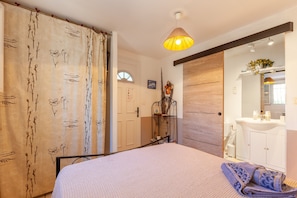 A bedroom with a bed, a bedside table, a hanging lamp, a window, and a bathroom with a sink and mirror.
