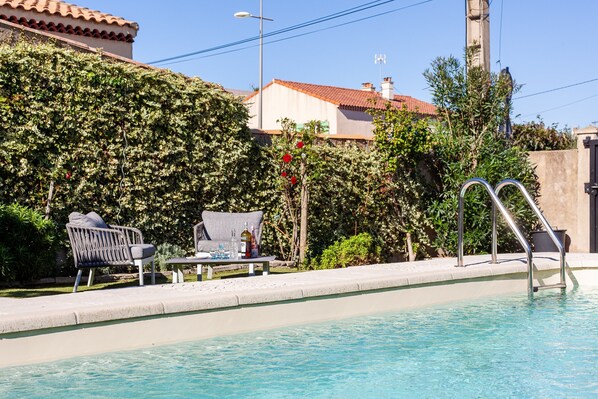 A swimming pool with a metal ladder, a chair, and a table with bottles. - Salamandre Guest Room with Shared Pool, Wi-Fi, and Air Conditioning (Port-Saint-Louis-du-Rhône)
