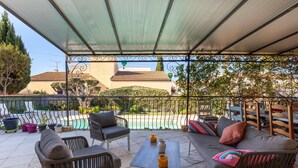 A covered outdoor seating area with a pool view, wicker furniture, and a metal railing. - Salamandre Guest Room with Shared Pool, Wi-Fi, and Air Conditioning (Port-Saint-Louis-du-Rhône)