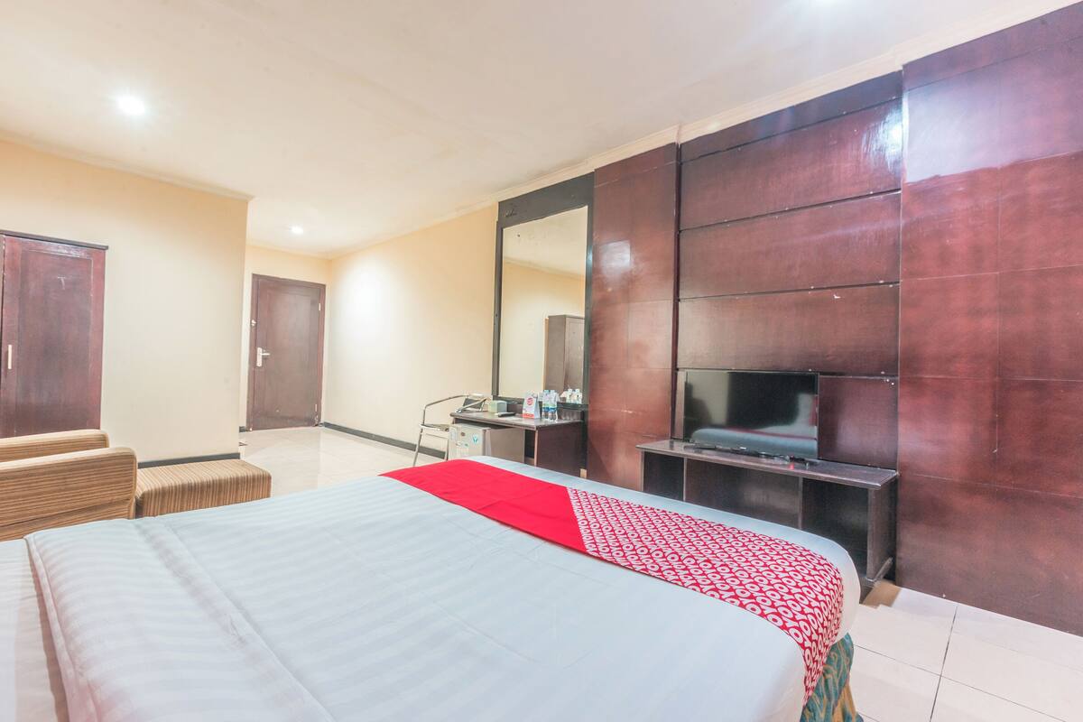 A hotel room with a bed, a desk, a chair, a TV, and a wardrobe.