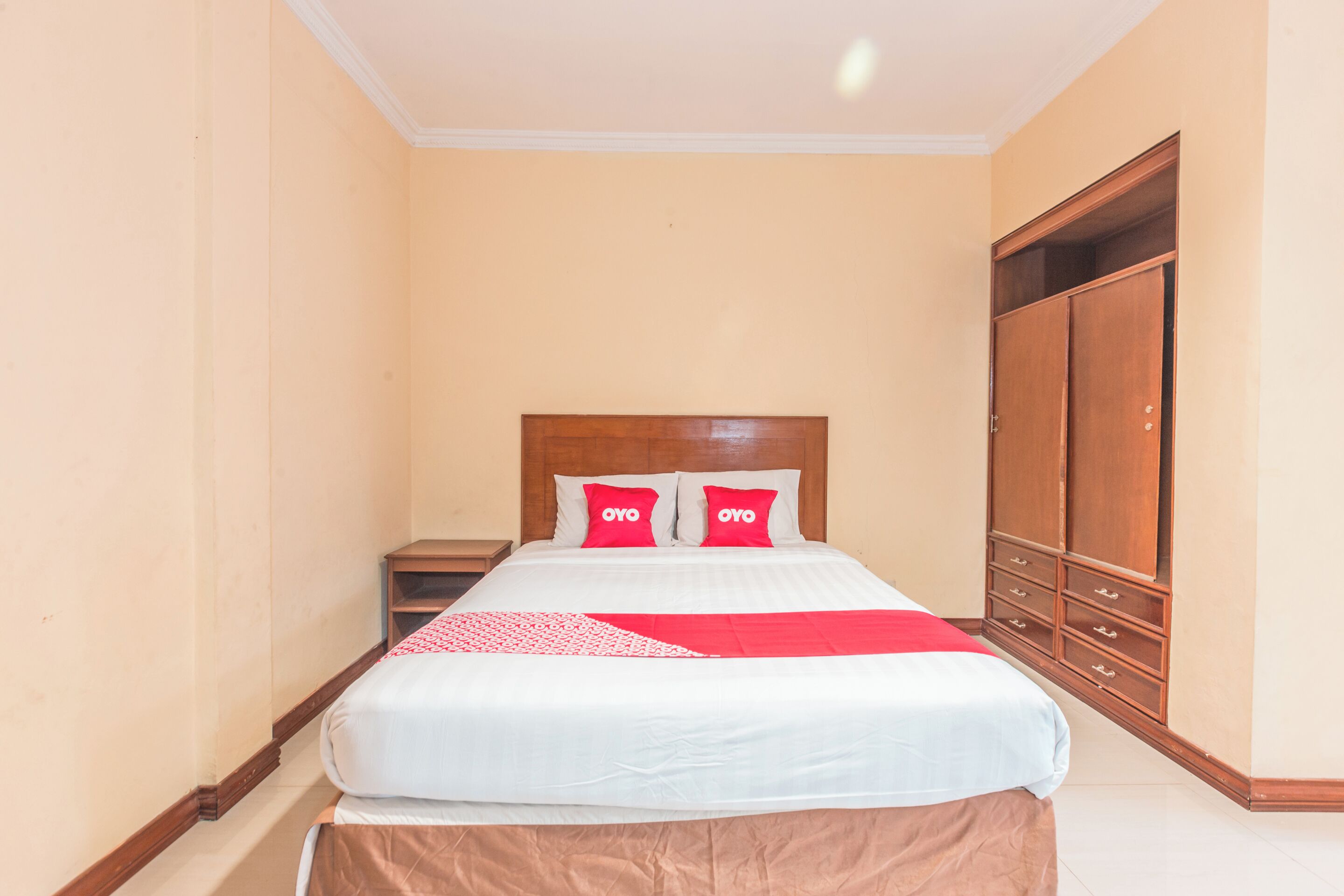 A neatly made bed with a wooden headboard, two red pillows, and a white bedspread.