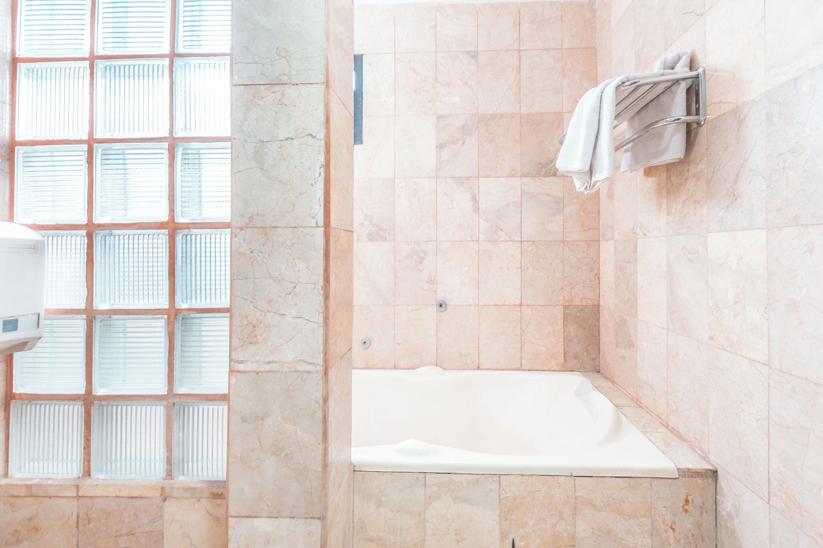Une salle de bain avec une baignoire, un porte-serviettes et une fenêtre avec des stores.