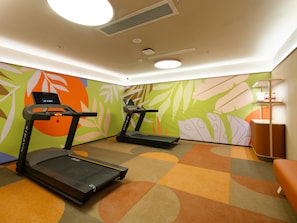 Un gimnasio con cintas de correr y una pared con diseño de hojas.