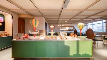 Un vestíbulo de hotel con un mostrador de recepción verde, una decoración con globo aerostático y un gran ventanal que ofrece vistas a la ciudad.