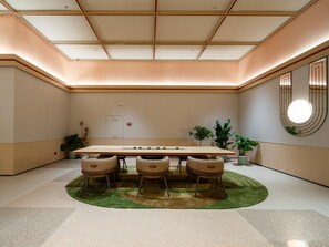 Una sala de conferencias con una gran mesa, cuatro sillas, alfombra verde y plantas en macetas.