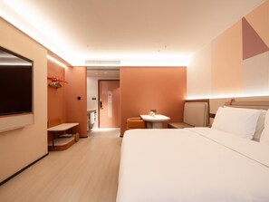 A hotel room with a bed, a small table, a TV, and a bathroom visible through an open door. - Orange Guangzhou Panyu Chimelong Wanbo Center (Guangzhou)