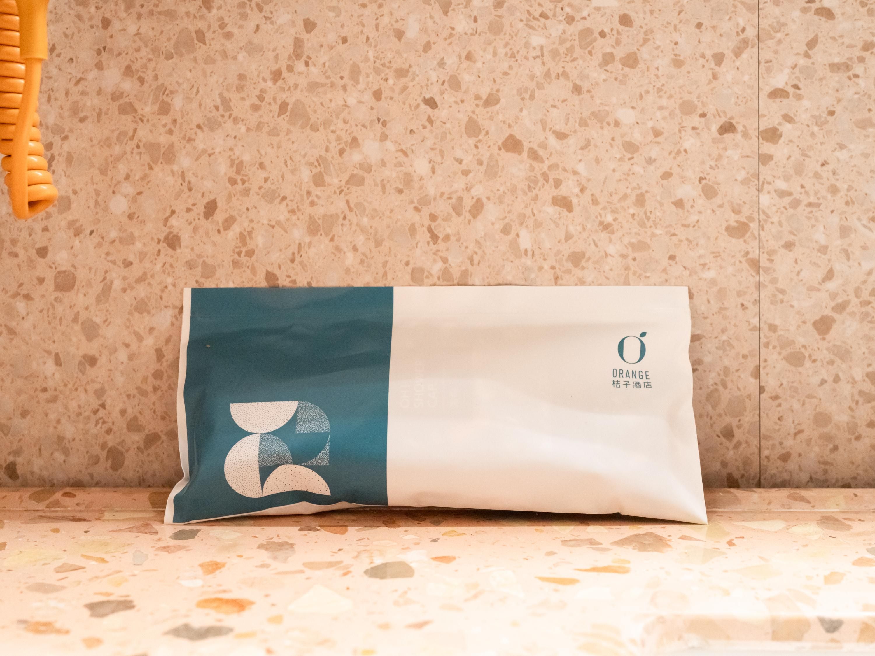 Uma embalagem com design azul-turquesa e branco, apoiada em uma superfície texturizada.