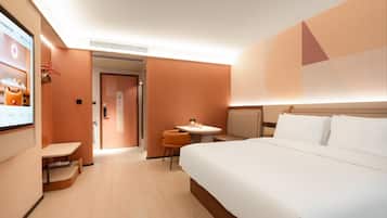Habitación de hotel con una cama grande, una mesita, una silla y una pantalla de televisión.