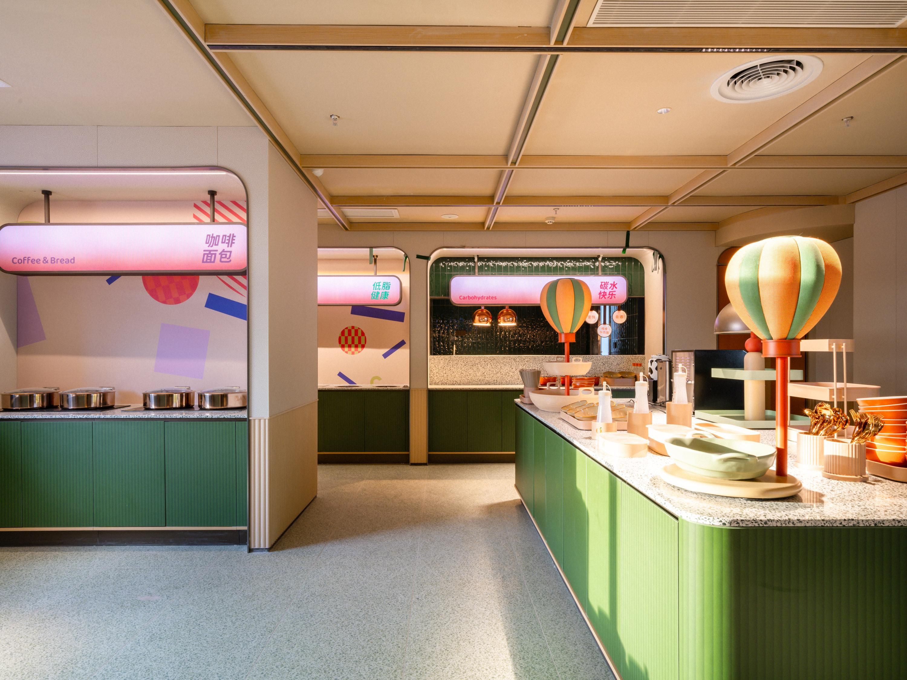 Interior moderno de una cafetería con armarios verdes, una barra con diversos productos y una pared mostrando opciones de menú en varios idiomas.