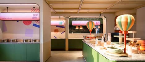 Interior moderno de una cafetería con armarios verdes, una barra con diversos productos y una pared mostrando opciones de menú en varios idiomas.