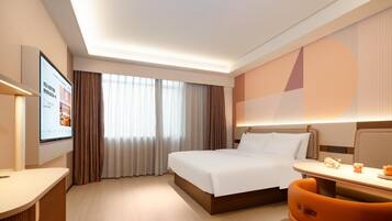 Quarto de hotel com cama, escrivaninha, cadeira, televisão e janela com cortinas.