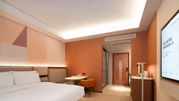 Quarto de hotel moderno com cama, escrivaninha, cadeira e televisão exibindo informações.