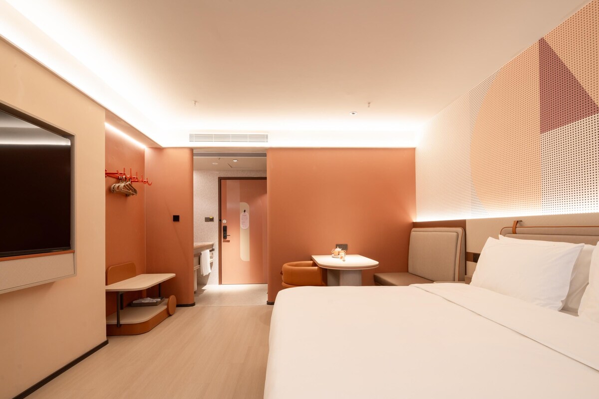 Habitación de hotel con cama, una mesita, televisión y baño visible a través de una puerta abierta.
