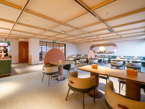 A modern interior with a high ceiling, multiple tables and chairs, and a large window providing natural light. - Orange Guangzhou Panyu Chimelong Wanbo Center (Guangzhou)