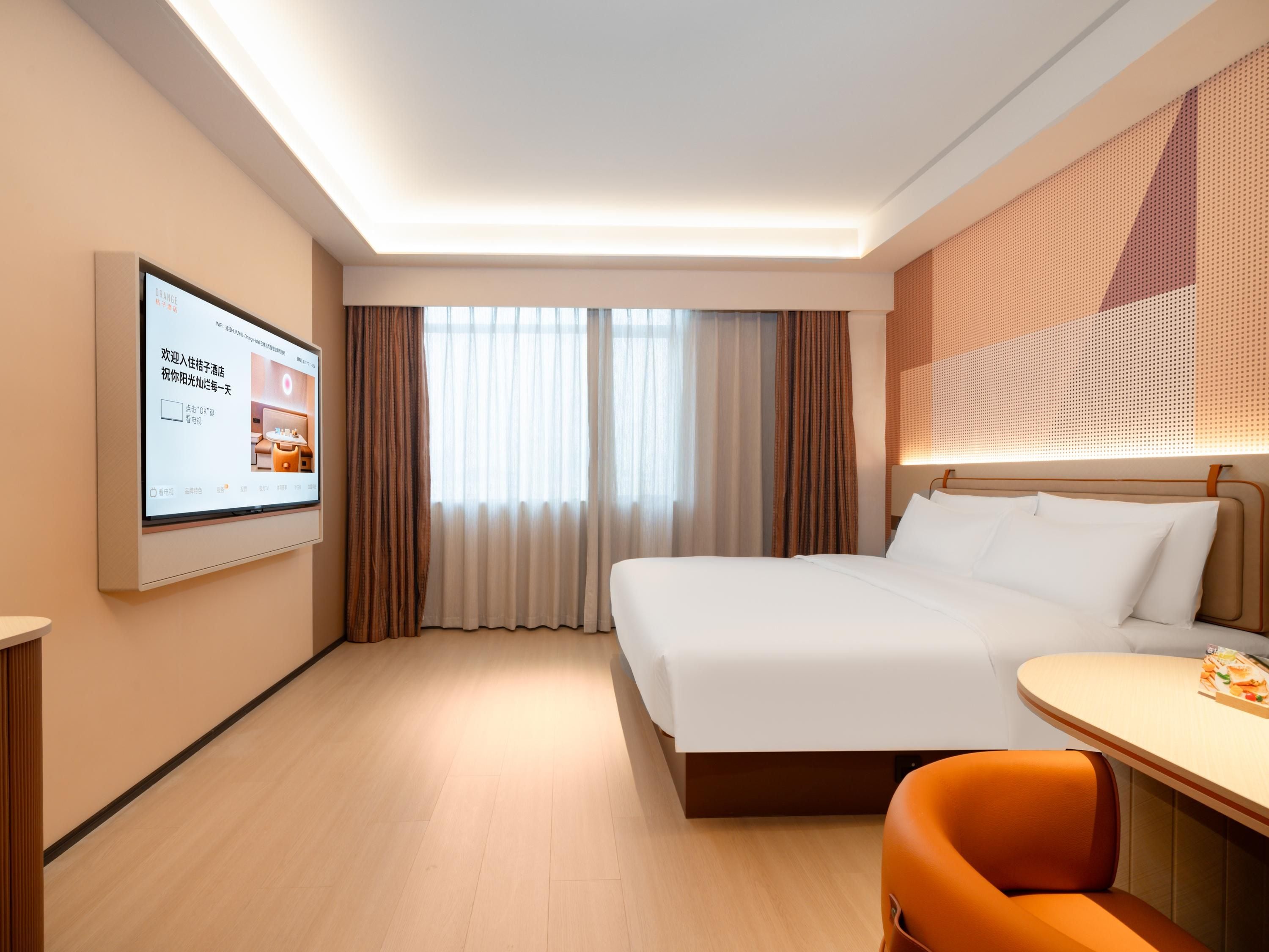 A hotel room with a bed, a desk with a chair, a television mounted on the wall, and a window with curtains.