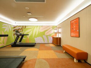 Un gimnasio con una cinta de correr, una banca, un mapa colgado en la pared y una alfombra estampada.