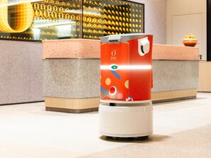 Un dispensador de bebidas autoservicio rojo y blanco con una etiqueta colorida en el vestíbulo de un hotel.