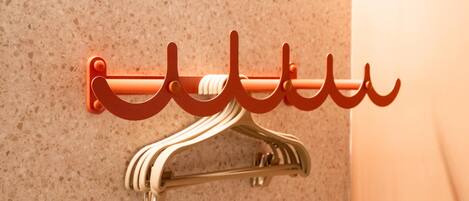 A wall-mounted coat rack with a metal hanger and a red hook.