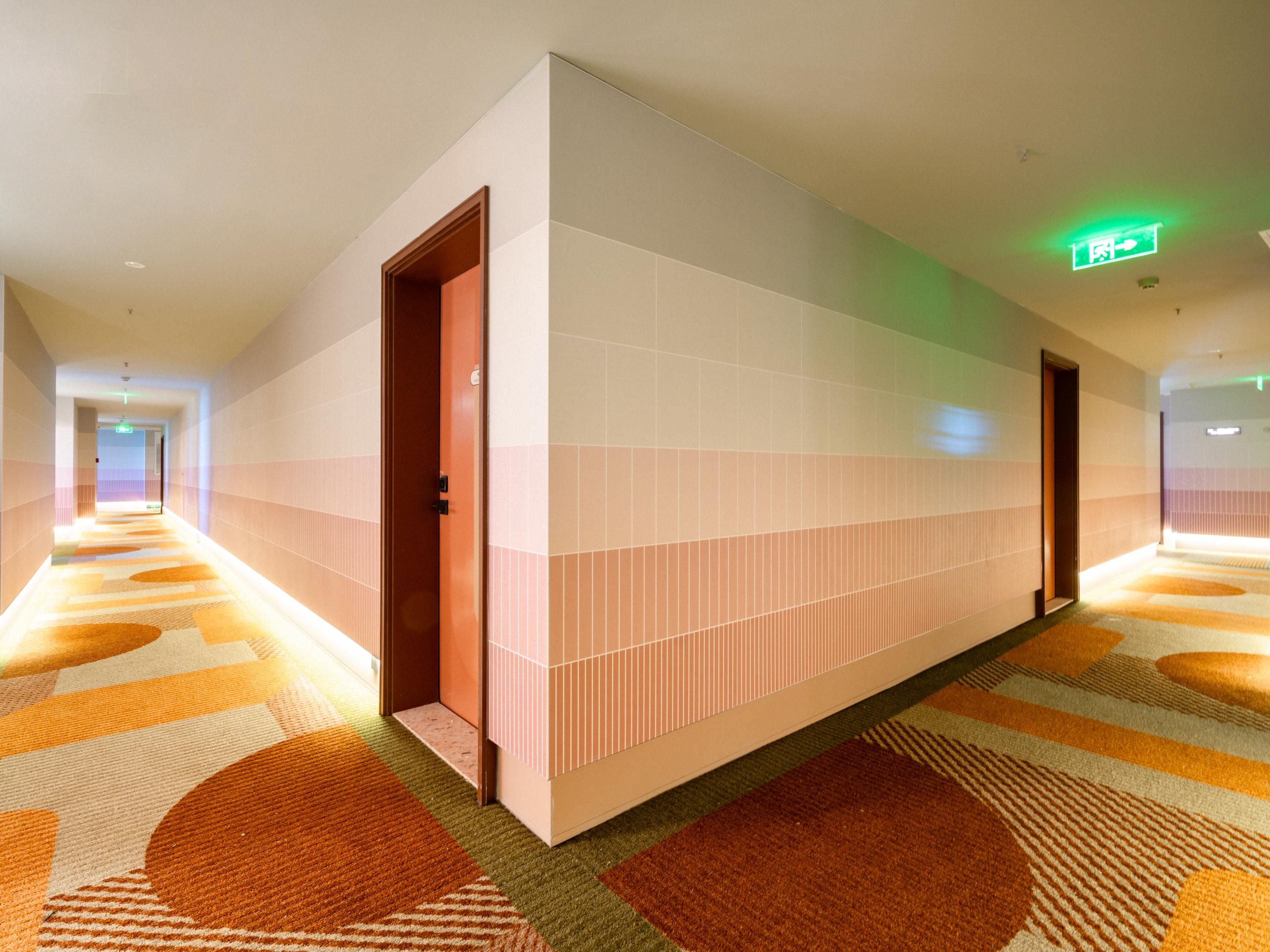 Ein Hotelkorridor mit Teppichboden, gefliesten Wänden und einer Holztür.