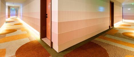 Un couloir d’hôtel avec un tapis à motifs, un mur recouvert de carreaux et une porte en bois.