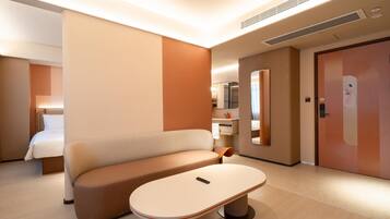 A modern hotel room with a sofa, a small table, a mirror, a bathroom, and a door.