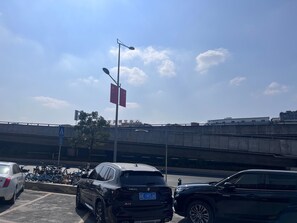 Un área de estacionamiento con automóviles y bicicletas, una señal de paso de peatones, y un asta con banderas.