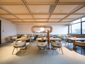 Una sala de conferencias moderna con techo alto, cabinas tapizadas en verde y un gran espejo circular en la pared.