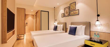 Habitación de hotel con dos camas, una mesita de noche con botellas de agua, un televisor y cuadros en la pared.